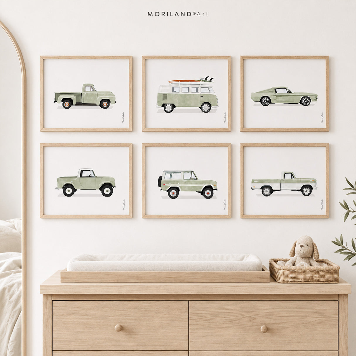 Set of six sage green vintage vehicle art prints in natural wood frames above a light wood nursery changing table.