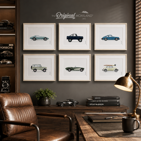Six vintage car art prints in light wood frames styled in a sophisticated home office with a leather chair, dark wood desk and automotive décor.