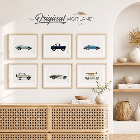 Set of six MORILAND classic car fine art paper prints in light wood frames, displayed in a bright neutral living room above a cane cabinet.