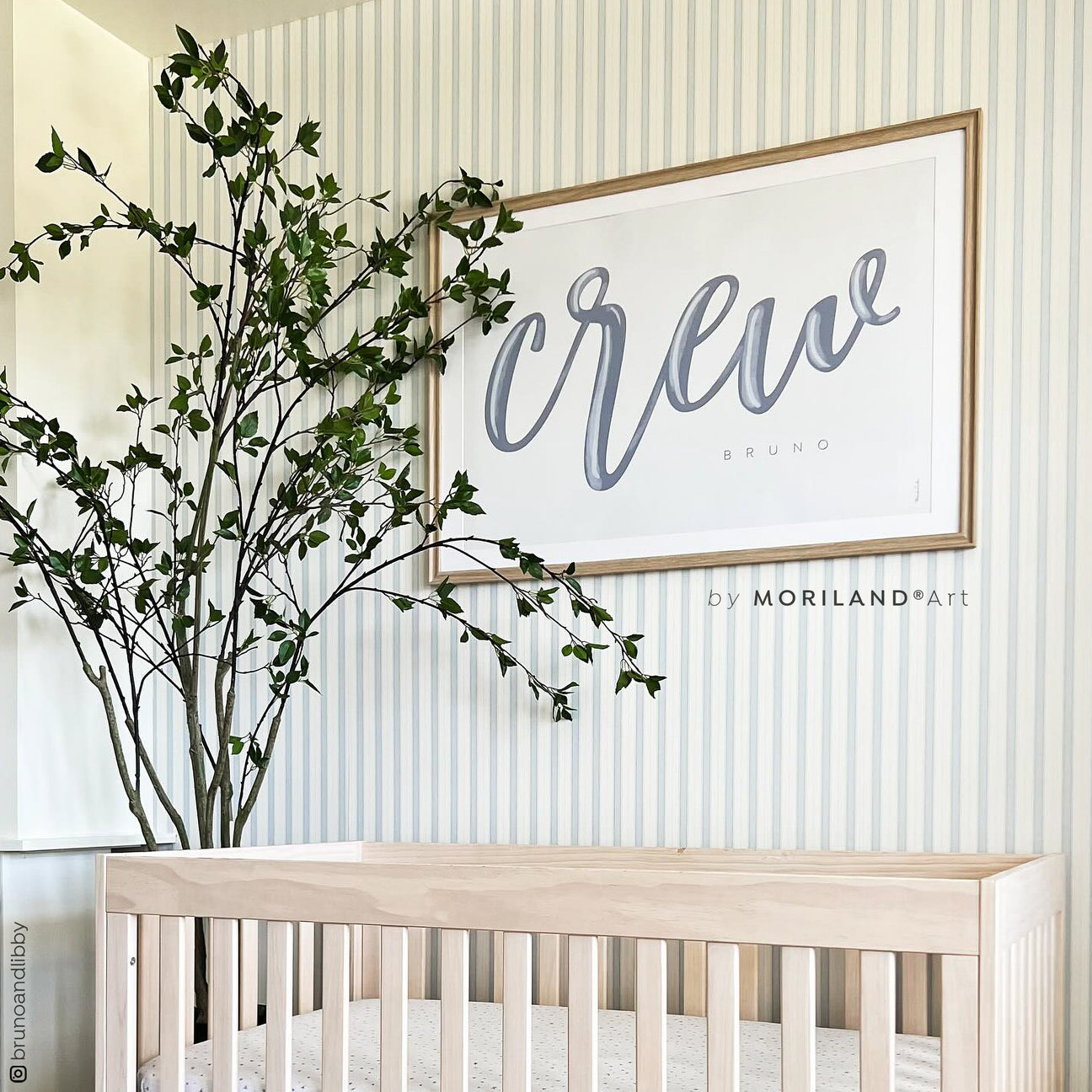 Personalized paint brush style name print featuring Anthony Michael in black, displayed in a slim wood frame above a cane cabinet.