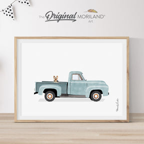 Modern heritage watercolor style illustration of a Yorkshire Terrier dog sitting in the bed of a pale blue vintage classic pickup truck, displayed in a light wood frame for a nursery or dog lover gift by MORILAND.