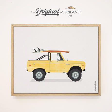 A minimalist watercolor art print of a classic yellow vintage Bronco truck with surfboards stacked flat on top, shown as a framed canvas product mockup in a natural oak frame.